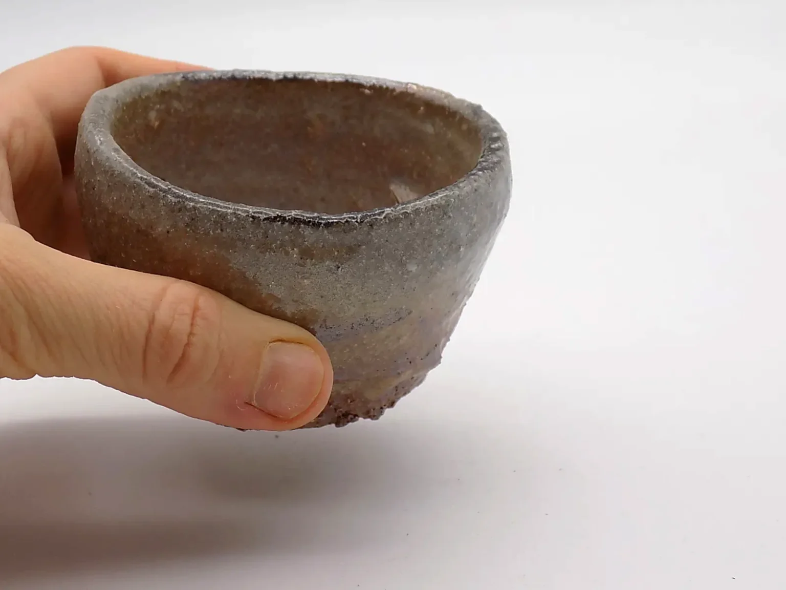 Rustic brown sake cup held in hand, top view 02 by Timi Lantos Ceramics