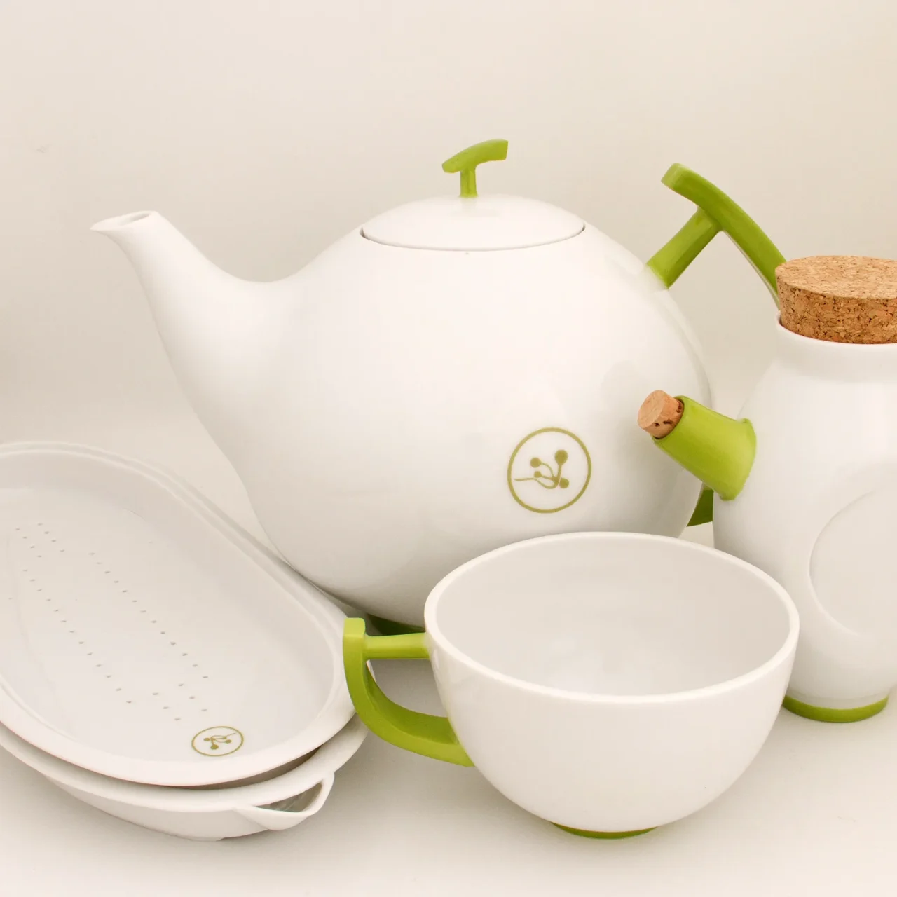 Minimalist white porcelain tea-session set with green handles, including teapot, cup, milk jug and serving trays on a white background